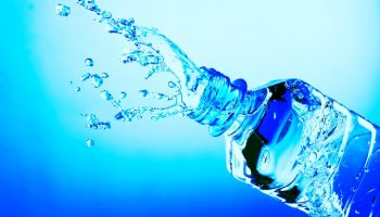 Water is seen splashing from a plastic water bottle against a sky blue background.