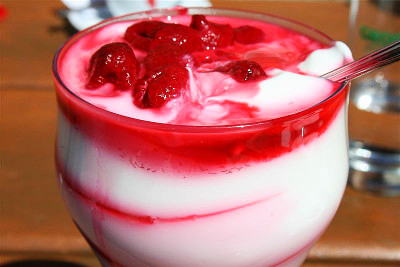 A clear dessert cup is hold yogurt with raspberry swirls throughout it with whole raspberries on top.